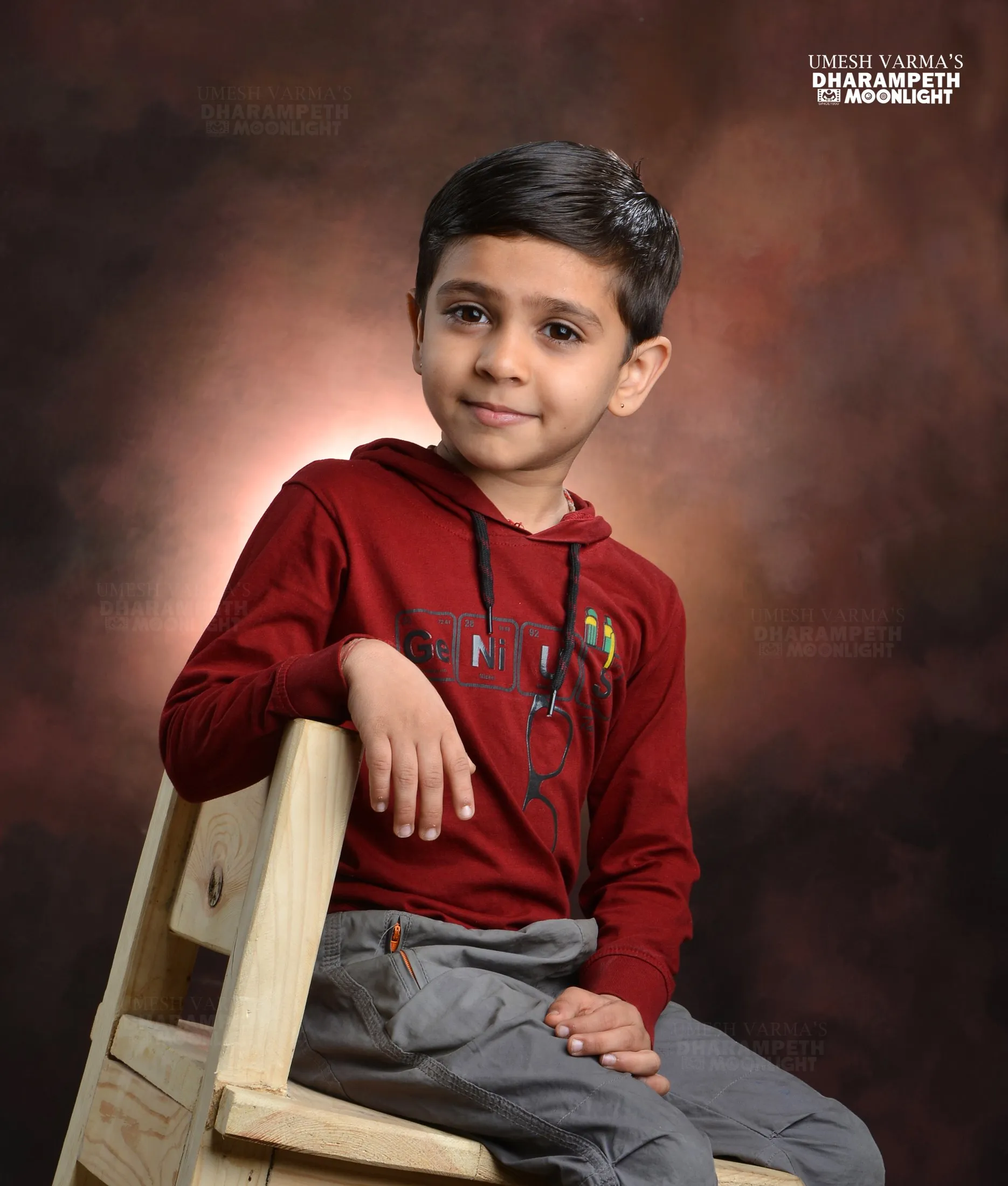Young boy in a red hoodie sitting on a wooden chair in the studio